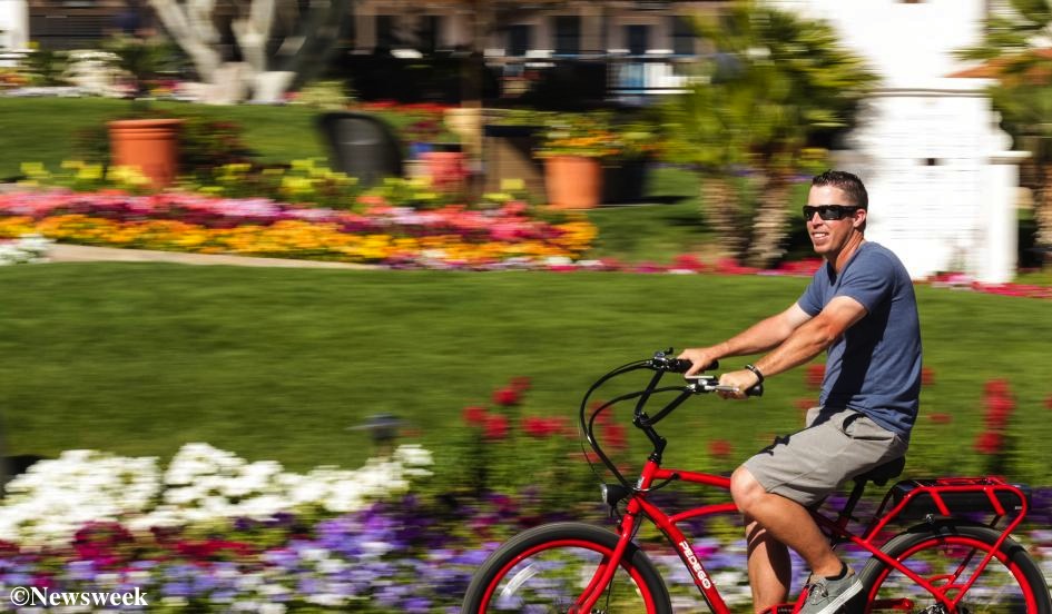 Man riding a red pedego electric bike through a flowered city park