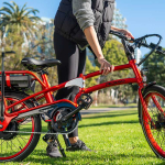 The new V2 Pedego Latch Folding Bike in red with a happy cyclist in an urban setting.