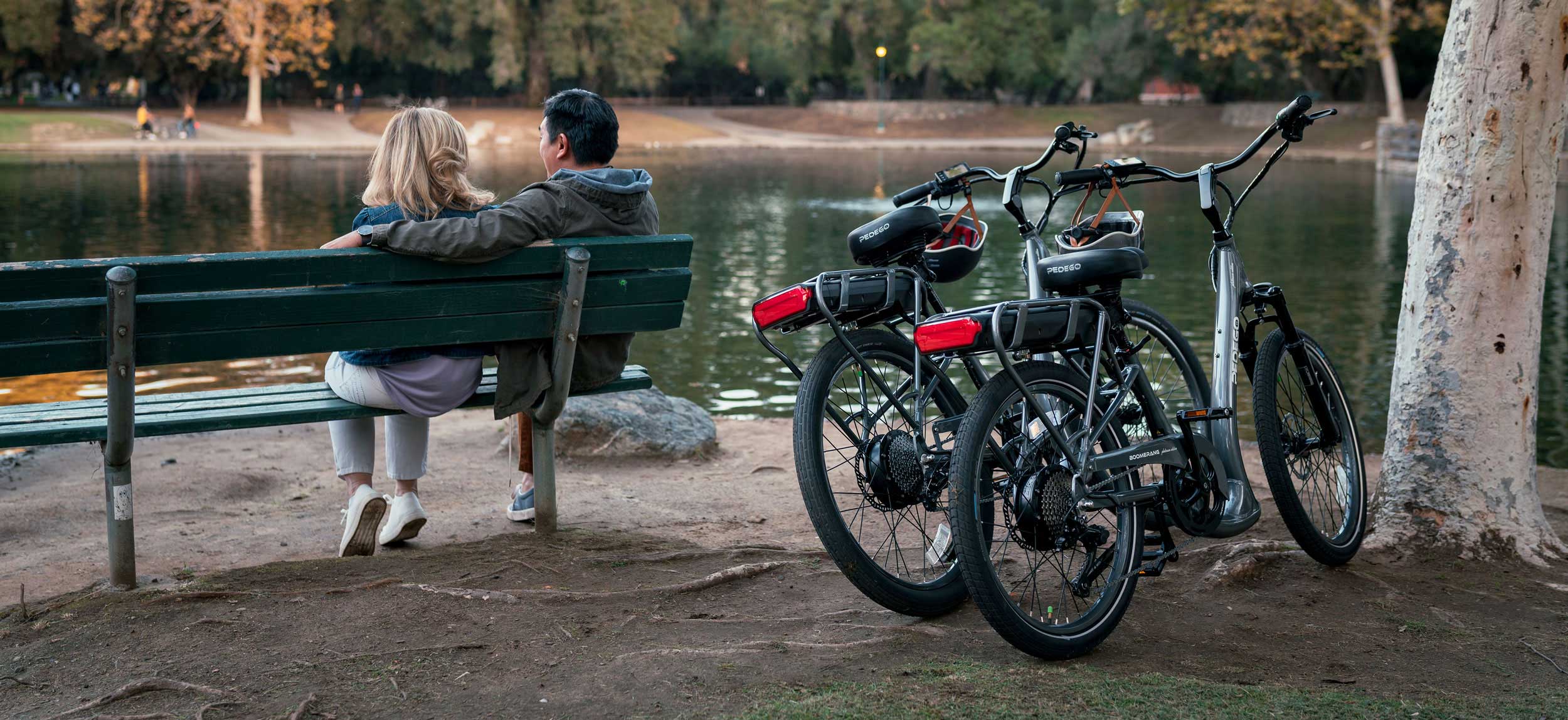 Couple sitting lakeside with pedego electric bikes parked