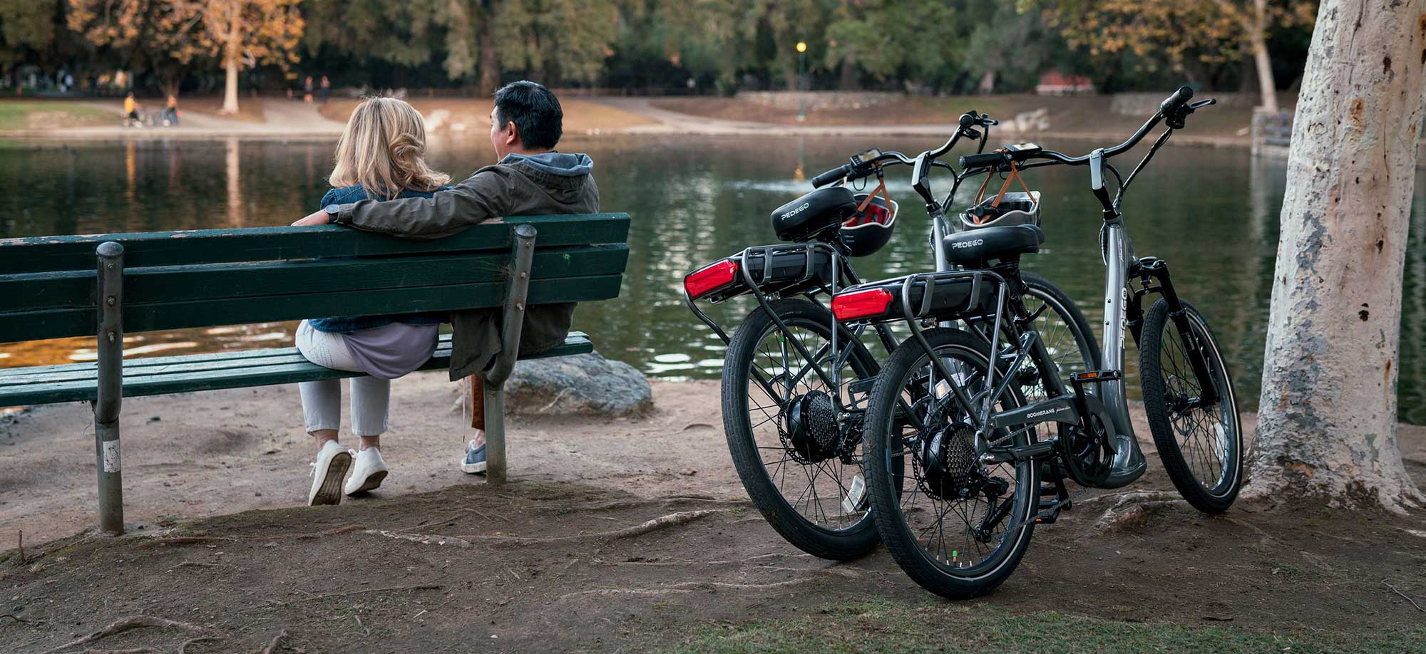 Couple sitting on a bench beside a lake with parked pedego bikes
