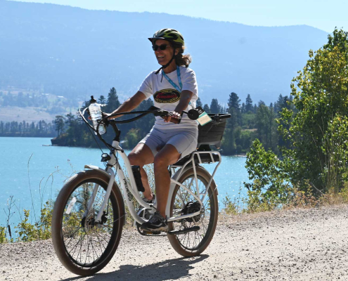 Happy woman riding white pedego electric bike on a lakeside trail.