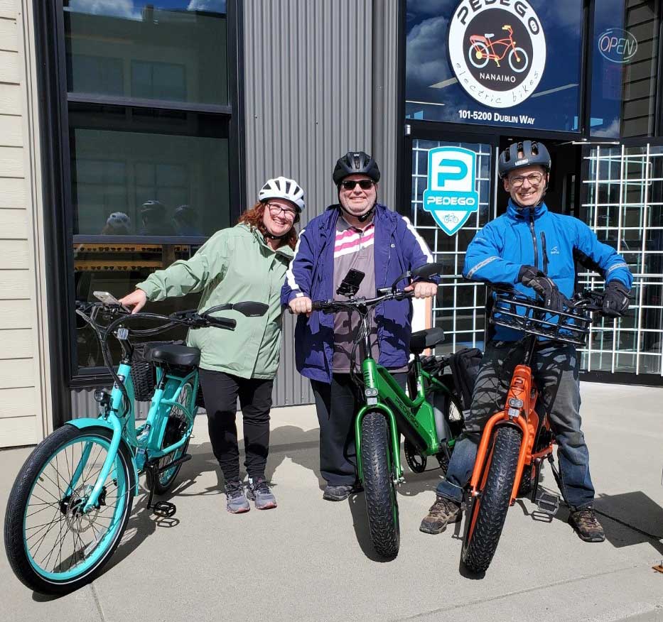 Three people with their pedego electric bikes outside the bike shop
