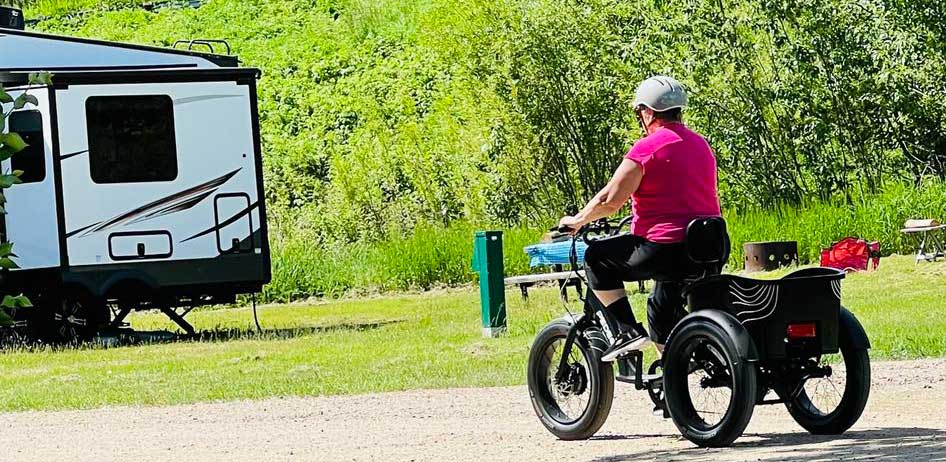 Person rides a Pedego Fat Tire Trike toward an rv at a campsite.